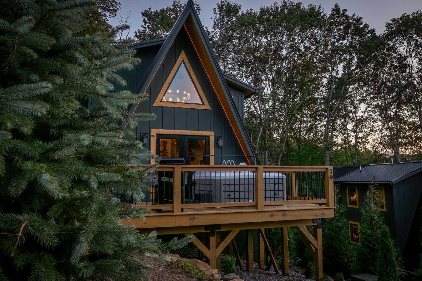 A-frame cabin with hot tub deck among the trees at dusk